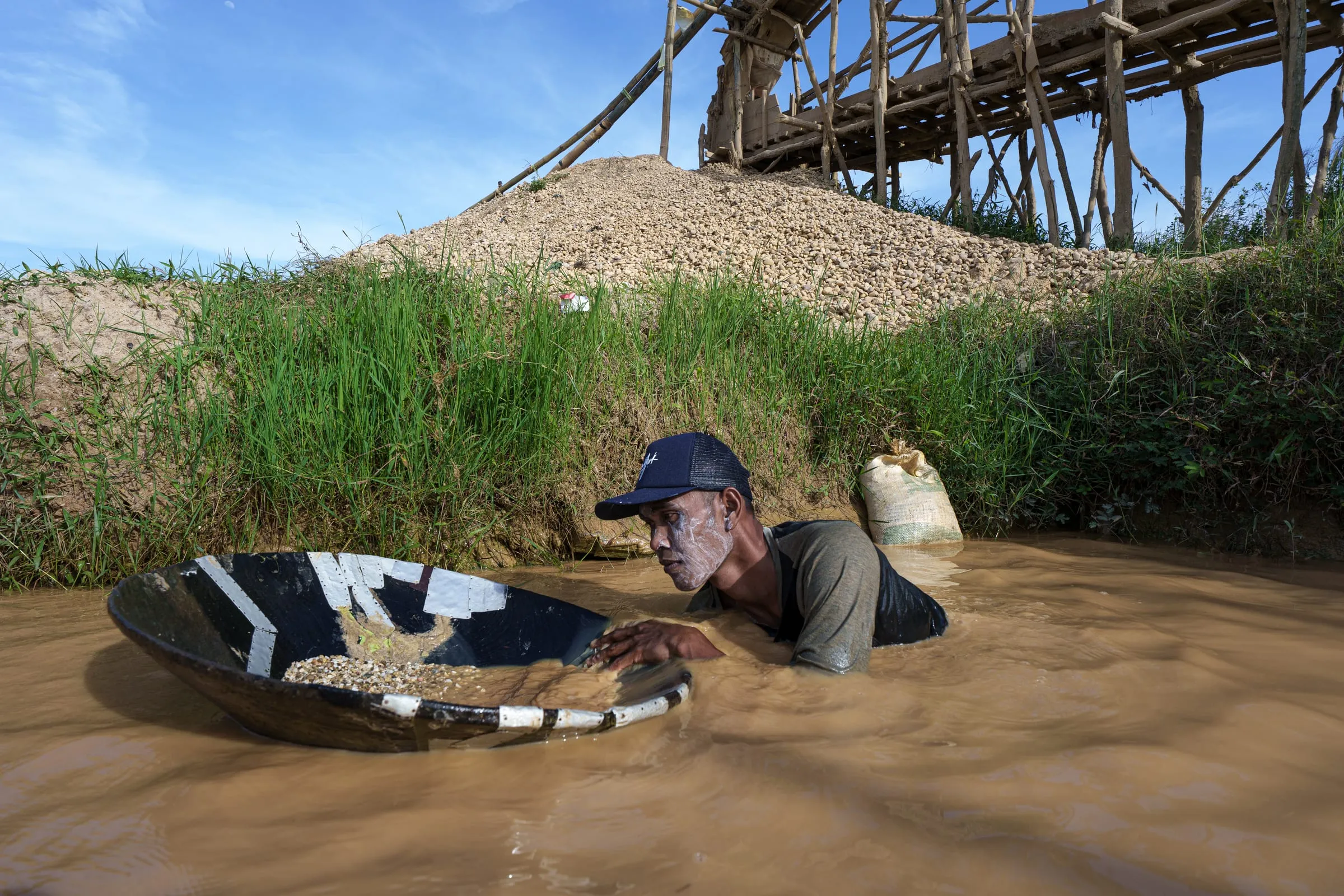 Mohammed, 38, searches for diamonds using a dulang — a shallow wooden pan carved from black ironwood. He began mining at 18, alongside his brother Amin. Each day, they sift through hundreds of baskets of gravel, often finding nothing.