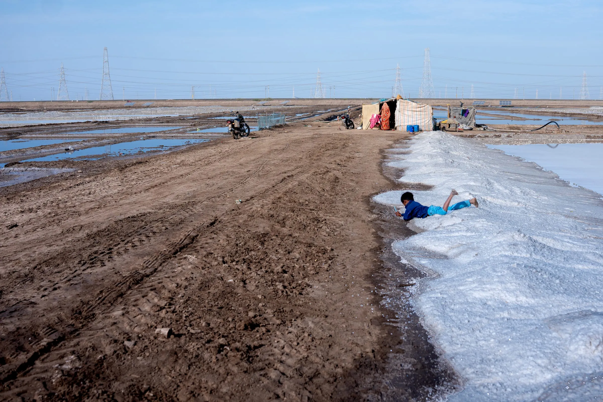 A child plays near the salt pools in Maliya, Gujarat, India. Salt workers migrate each year with their families to the salt pans during the harvest season, typically from October to March. Children from salt-working families often miss school due to this seasonal migration.